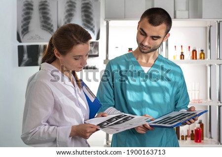 Two attentive doctors woman and man in medical apparel holding clip-folders and discussing MRI scan or ultrasound picture. Lifestyle outdoor scene