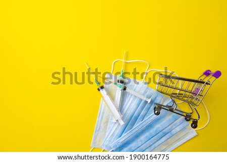 A shopping cart and medical syringes on a yellow background with copy space. Coronavirus, flu virus, epidemic. Vaccine.
