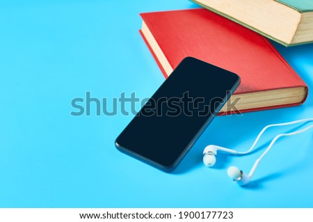 Smartphone with headphone and old books on blue background. Audiobook concept. Online education. E-learning. Modern technology