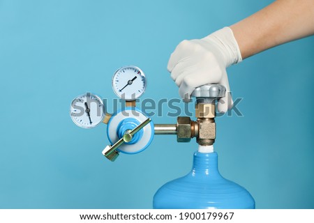 Medical worker checking oxygen tank on light blue background, closeup Royalty-Free Stock Photo #1900179967