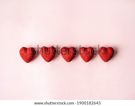 Five red shiny hearts on a pink background. Valentine's day concept. Top view. Copy space. Selective focus