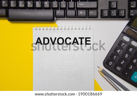 the word advocate is written on a yellow and white background near a computer keyboard and calculator. High quality photo