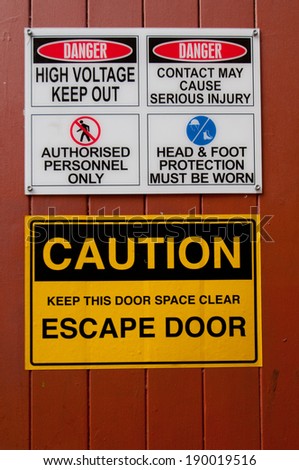 Yellow and black escape door sign and other warning signs on a building exterior