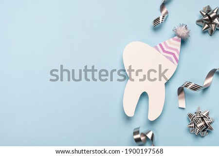 Decorative model tooth in a festive cap on light blue background. Dentist day, birthday or sale. Creative medical postcard for dentistry. Top view, flat lay, copy space