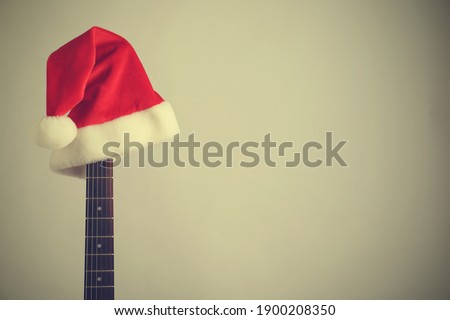 Guitar with Santa hat on light background, space for text. Christmas music