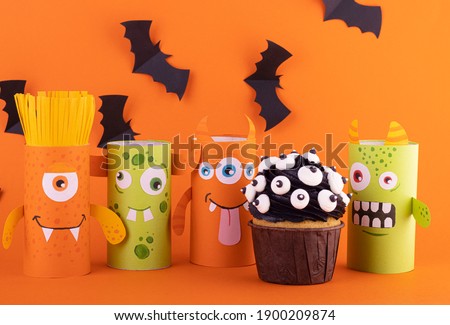 Paper ghost, a scary handmade monster with a black cupcake on an orange background with black spiders. The concept of Halloween crafts, DIY, creative toilet tube