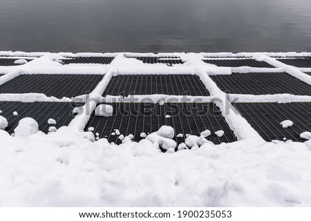 The photo shows an empty harbor dock partially covered with snow. The marina has a metal texture. in the background you can see a blurry sea. The scene exudes calmness.