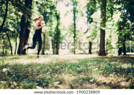 Blurred picture of sportswoman running in a nature on sunny day.