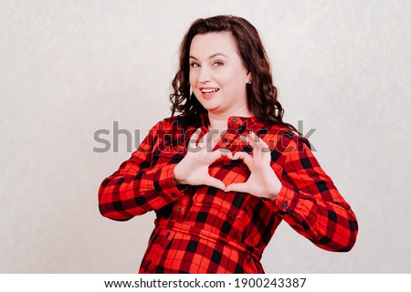 Attractive brunette woman in red checkered dress folded her fingers into heart shapes. declaration of love. Special offers for regular customers. cope space. valentine's day