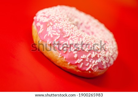 Cake donut with caramel and pink glaze, red background.