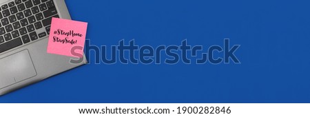 New normal 2021 workplace flat lay banner, stay home work concept, laptop and sheet of paper with a text, hashtag, blue background with a copy space photo