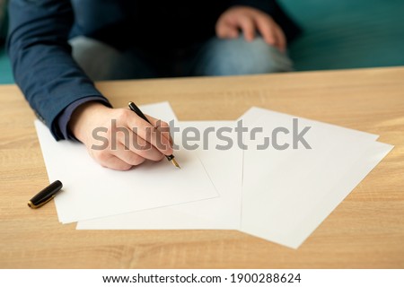 Businessman in the office writes a letter or signs a document on a piece of white paper with a fountain pen with nib. Closeup of hands of a businessman in a suit.