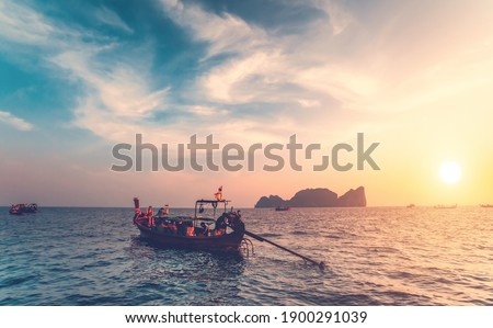 Thailand ocean boats cruise: people traveling on water transport at sun setting tones. Majestic sunset tourist vacation at waterfront. Mountain island silhouette at skyline under cloudy sky