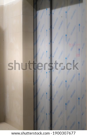 Blurry photo of a modern elevator with stickers closed doors in a empty floor. Store, interior, new building.