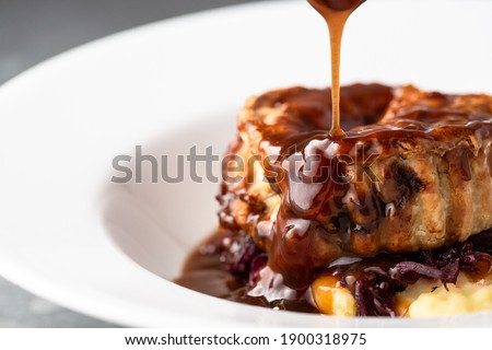 Gravy being poured onto a meat pie Royalty-Free Stock Photo #1900318975
