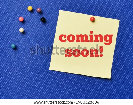 Text COMING SOON written on yellow paper note with pin board over blue background.Business concept.