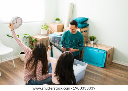 Young parents and daughter unpacking from a plastic container box after moving into a new house. Hispanic family deciding where to put their stuff and furniture