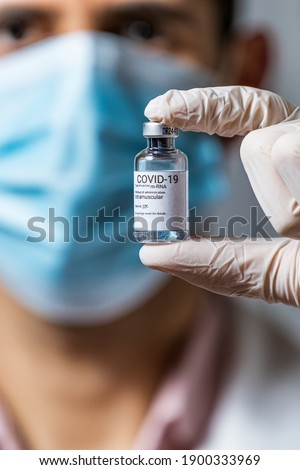 Covid 19 vaccine. Doctor or nurse or scientist with PPE (mask and gloves and gown) holding a syringe and the COVID-19 or Sars CoV 2 vaccine. Royalty-Free Stock Photo #1900333969
