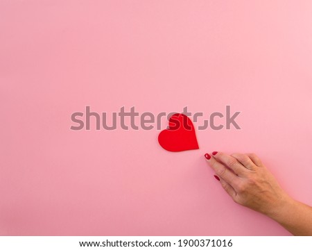 Woman hand pointing finger red heart, pink background, copy space. Flat lay, hand and present box, top view. Valentine or love, spring holidays, Christmas and birthday concept.