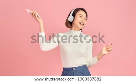 Happiness Asian smiling young woman wearing technology wireless headphones for listening the music via smart mobile phone Royalty-Free Stock Photo #1900387882