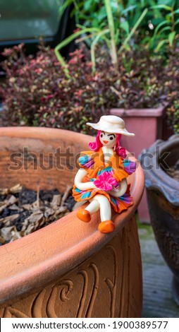 A girl doll resting on a plant pot