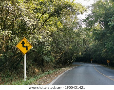 yellow curved direction sign on the ground with the beautiful green nature road mountain view.
