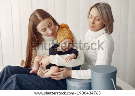 Family at home. Grandmother with daughter and grandson. Women in a white sweaters. Little kid in a cute yellow hat.