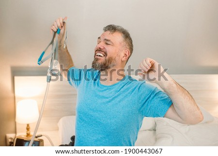 Happy rested man with chronic breathing issues after using  CPAP machine sitting on the bed in bedroom. Healthcare, CPAP, Obstructive sleep apnea therapy, snoring concept Royalty-Free Stock Photo #1900443067