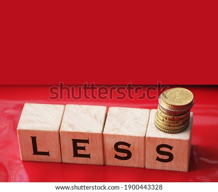 Less word on wooden cubic blocks with letters and stack of coins on it on red background. Business concept.