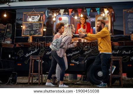 group of multiethnic young people having fun while eating in front of modified truck for mobile fast food service Royalty-Free Stock Photo #1900451038