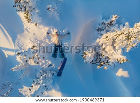 Snow angel, girl snowboarder lies with snowboard in winter forest, aerial top view.