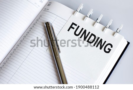 text FUNDING on short note texture background with pen