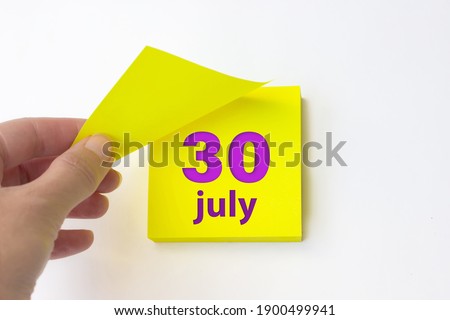 July 30th. Day 30 of month, Calendar date. Hand rips off the yellow sheet of the calendar. Summer month, day of the year concept