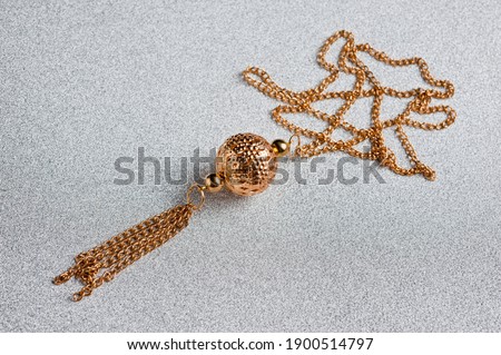 Jewelry in the form of a chain with a pendant in the form of a ball, gilded metal, photographed against a silver background.