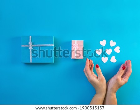 Gifts decorated with ribbon on blue background, woman hands hold small hearts. Valentine, spring holidays, Christmas, birthday concept. Flat lay, blue and pink present boxes, top view. 