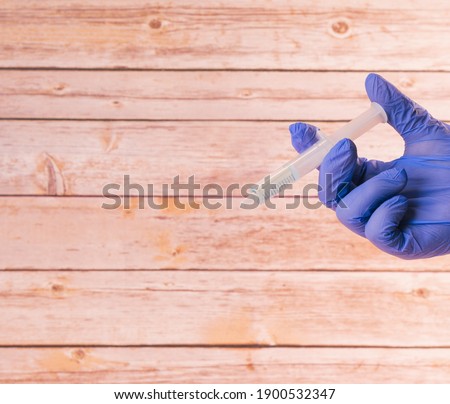 hand with a hospital latex glove by taking a syringe with the covid-19 vaccine with a wooden background.