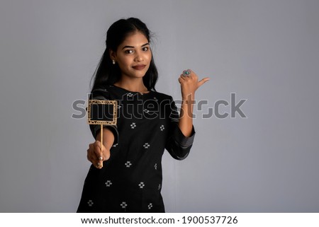 A young woman or businesswoman holding a little cutout board in her hands on a gray background.