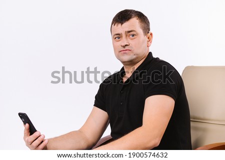Portrait of a hard of hearing man sitting in a office leather armchair with a smartphone. White background with empty space.