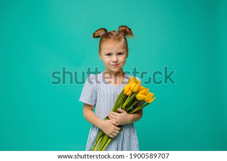 portrait of a little girl with two muzzles on her head and a bouquet of yellow tulips on a blue background with space for text
