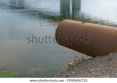 Metal pipe on the shore by the reservoir. The concept of a drain pipe, pollution of the river, pond.