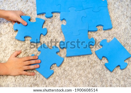 The child's hands put together large puzzles on the carpet. Games for children that develop intelligence and logic. Details without pictures. Beyond recognition