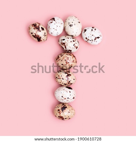 Letter T from Easter Quail eggs pink colored. Spring Easter composition with chocolate food. Monochrome image, minimal style. Top view
