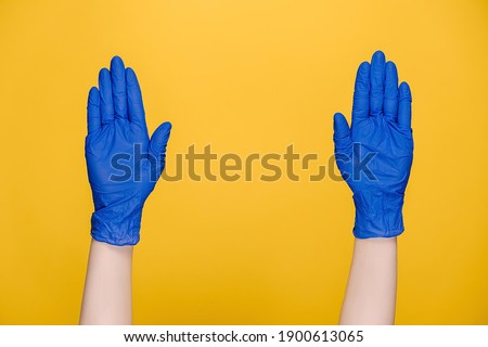 Close up of male hands in medical protective blue gloves snaps her fingers to music rhythm gesture, isolated over yellow wall in studio. Copy space for advertisement. With place for text or image