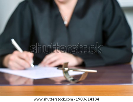 Concept: Female lawyer, out of focus in the background, researching in black robe and works in her office. All blurred! Royalty-Free Stock Photo #1900614184