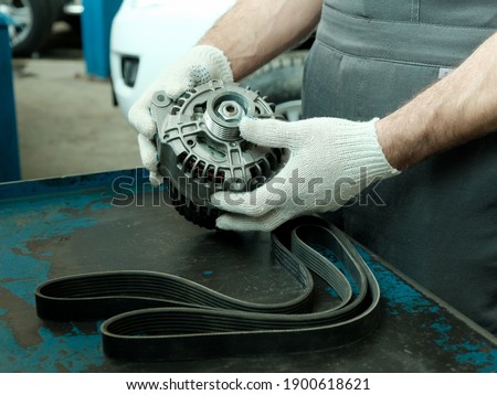 Car parts close-up on the desktop.The mechanic inspects the generator and the drive belt of the internal combustion engine units before installation during the repair of the car in the service center Royalty-Free Stock Photo #1900618621