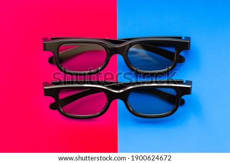 3D glasses for watching movies in the cinema and at home on a pink-blue background close-up, two pairs of black 3D glasses