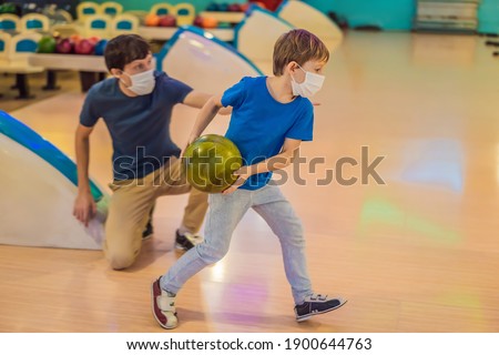 Father and son playing bowling with medical masks during COVID-19 coronavirus in bowling club