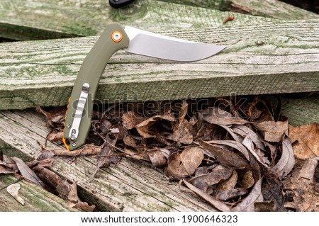 Green knife handle on a green tree. Knife with a clip for carrying. Angle view.