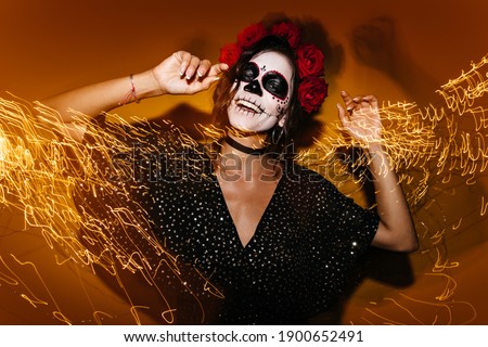 Portrait of unusual girl in midst of party. Model with skull mask dances and poses on lights background