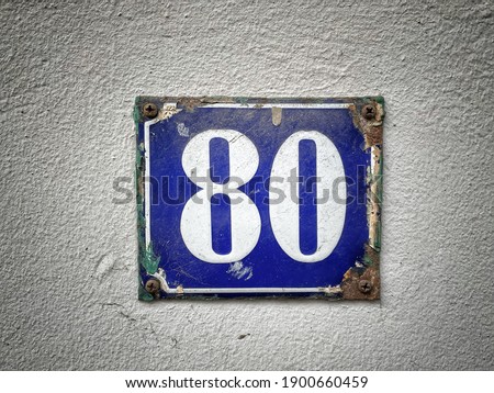 Number 80, the number of houses, apartments, streets. The white number on a blue metal plate, house number eighty (80) on a rough wall.
